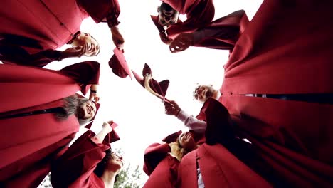 Slow-motion-low-angle-shot-of-graduates-standing-in-circle-throwing-mortar-boards-in-the-sky-and-laughing.-Togetherness,-friendship-and-modern-lifestyle-concept.