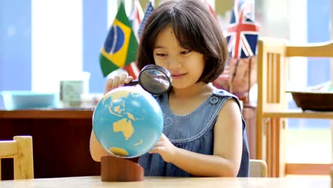 4K-Little-Asian-student-looking-at-globe-with-magnifying-glass