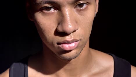 Young-handsome-african-man-with-pierced-ear-looking-at-camera-with-serious-expression,-black-background