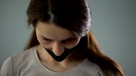 Bruised-woman-with-taped-mouth-sadly-looking-into-camera,-victim-of-abuse