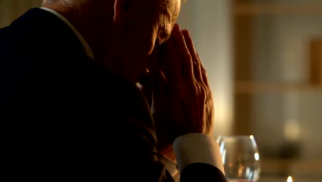 Senior-man-praying-at-table-before-festive-dinner,-remembering-passed-away-wife