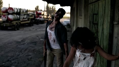 Halloween-horror-filming-concept.-Picture-of-creepy-male-and-female-ghost-or-zombie-walking-with-wounded-face-and-bloody-clothes.-Industrial,-abandoned-town-and-tracks-on-the-background