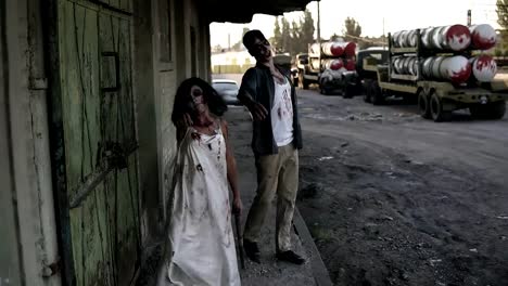 Portrait-of-creepy-male-and-female-ghost-or-zombie-walking-with-wounded-face-and-bloody-clothes.-Man-holding-saw-and-woman-is-with-a-stick.-Industrial,-abandoned-town-and-tracks-on-the-background