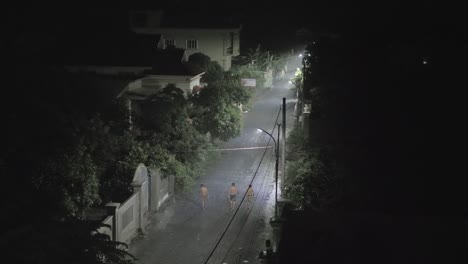 siluetas-de-hombres-a-pie-en-la-pequeña-calle-por-la-noche-mientras-llueve