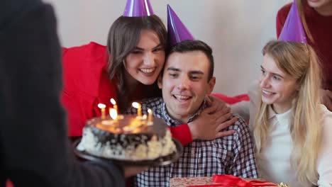 Handsome-man-blowing-birthday-candles-while-close-friends-throwing-a-surprise-party,-slowmotion-in-cozy-modern-apartment