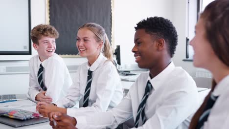 Línea-de-estudiantes-de-secundaria-con-uniforme-sentado-en-el-escritorio-en-aula-riendo