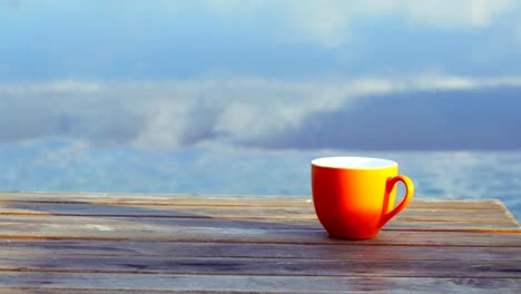 Orange-auf-Tasse-Kaffee-braun-Holztisch-am-Strand-mit-Brandung-des-Meeres-im-Hintergrund.