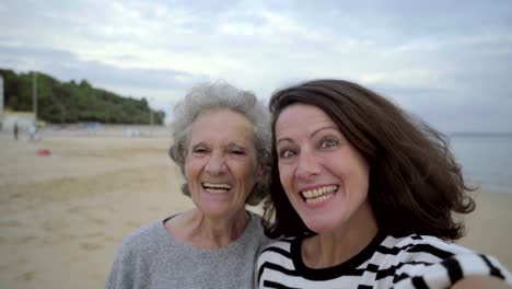 Adult-cheerful-daughter-kissing-senior-mom-and-taking-selfie