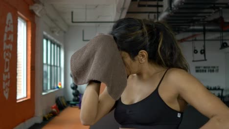 Attractive-fit-female-athlete-woman-wiping-sweat-after-intensive-exercise-training-in-fitness-gym.-Shot-in-slow-motion.