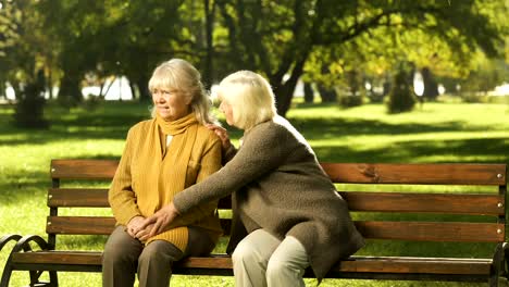 Senior-lady-comforting-old-friend-about-her-loss,-sitting-on-bench-in-park