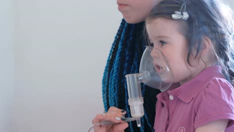 Kleine-süße-Mädchen-mit-ihrer-Mutter-durch-Inhalator-Maske-einatmen.-Verwenden-Sie-Vernebler-und-Inhalator-für-die-Behandlung.