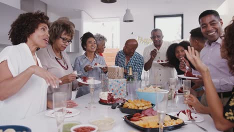 Tres-generación-de-la-familia-negra-de-pie-alrededor-de-una-mesa-comiendo-pastel-y-en-una-fiesta-de-cumpleaños-familiar