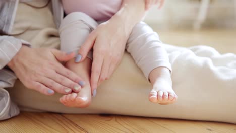 Madre-amante-irreconocible-acariciando-suavemente-pequeños-pies-de-linda-hija-bebé-sentado-en-su-regazo