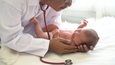 4K-Video-Selective-focus-medium-shot-of-male-doctor-examining--newborn-baby-girl-laying-down-on-white-bed-and-crying-by-use-stethoscope-listening-to-heartbeat