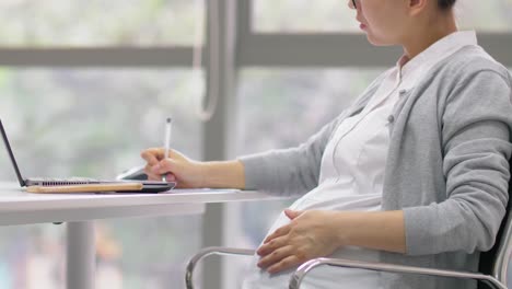 Chinese-pregnant-office-woman-is-working-with-laptop-and-documents