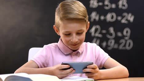 Little-boy-playing-video-game-on-smartphone-during-school-lesson,-bad-pupil