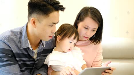 Asian-parents-father-and-mother-and-daughter-playing-with-digital-tablet-on-sofa