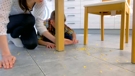 Mama-schimpft-ihren-Sohn-für-verstreutes-Essen-auf-dem-Küchenboden-und-lässt-ihn-aufräumen.