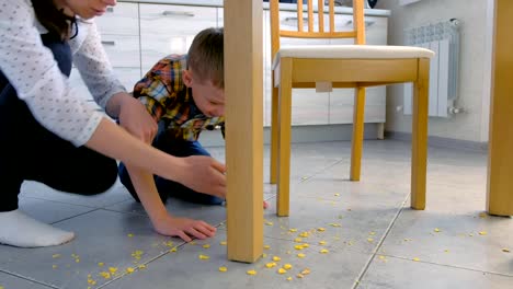 Mamá-regaña-a-su-hijo-por-comida-dispersa-en-el-piso-de-la-cocina-y-lo-hace-limpiar.