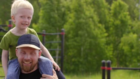 Sudoroso-caucásico-papá-posando-con-hijo-pequeño-en-el-gimnasio-al-aire-libre