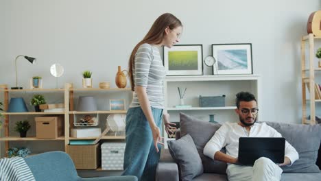 Man-using-laptop-on-sofa-at-home-while-angry-woman-yelling-at-him