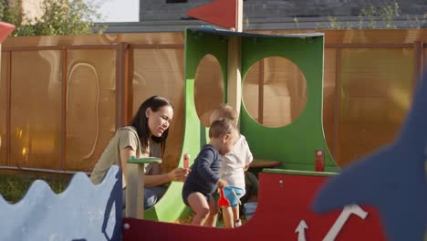 Junge-asiatische-Frau-sucht-nach-drei-Kleinkindern-in-Sandbox