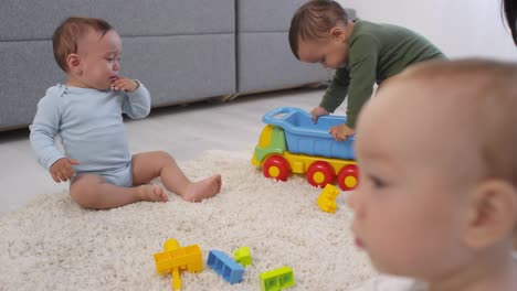 Three-Toddlers-Playing-on-Carpet-at-Home-and-Mom-Watching