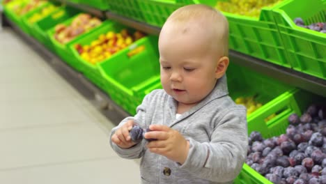 Nettes-Kleinkind-nimmt-Pflaumen-im-Supermarkt