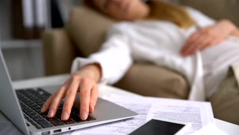 Tired-young-businesswoman-sleeping-on-the-couch-in-the-office-with-laptop.-Close-up-of-her-hand-on-the-keyboard