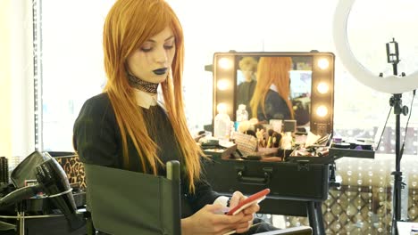 Hermosa-joven-con-maquillaje-de-halloween-utilizando-teléfonos-inteligentes-en-el-salón-de-belleza