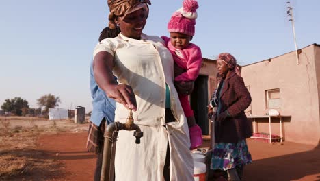 Mujer-africana-que-habla-a-su-bebé-durante-el-llenado-de-la-cubeta-de-agua