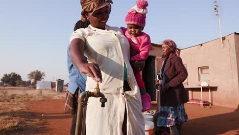 Afrikanische-Frau-im-Gespräch-mit-ihrem-Baby-während-der-Eimer-mit-Wasser-füllen