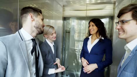 Tracking-shot-of-Businesswomen-and-businessmen-colleagues-talking-in-moving-elevator-and-come-out-from-it-and-walking-in-hall-in-modern-business-center
