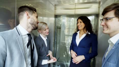 Tiro-de-seguimiento-de-mujeres-empresarias-y-empresarios-colegas-hablando-en-el-movimiento-del-elevador-y-salen-de-él-y-caminar-en-el-hall-de-moderno-centro-de-negocios