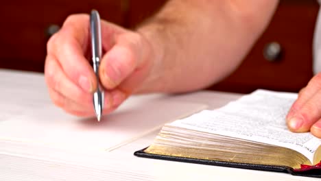 Hombre-sostiene-una-pluma-en-su-mano-con-un-libro-abierto-en-frente-de-él