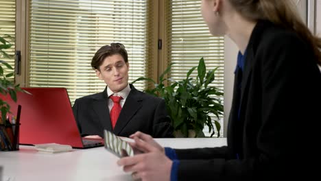 A-young-guy-in-a-suit-shows-a-heart-sign-to-a-female-employee.-Sign-of-love,-flirting,-work-in-the-office-concept.-60-fps