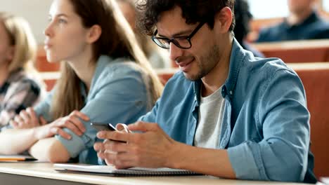 Hispanic-Mann-nutzt-Smartphone-während-einer-Vorlesung-im-Klassenzimmer.-Junge-helle-Studenten-studieren-an-der-Universität.