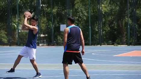 adultos-jóvenes-asiáticos-jugando-baloncesto-en-la-cancha-al-aire-libre