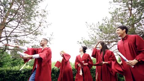 Low-shot-of-happy-graduates-throwing-mortarboards-in-air,-laughing-and-celebrating-graduation-on-college-campus.-Education,-success-and-modern-youth-concept.