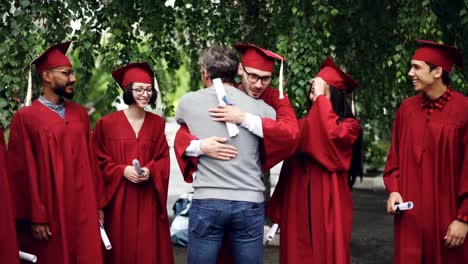 Slow-motion-of-proud-university-teacher-hugging-his-students-and-shaking-hands,-graduating-students-are-standing-in-line-with-diplomas-and-laughing.