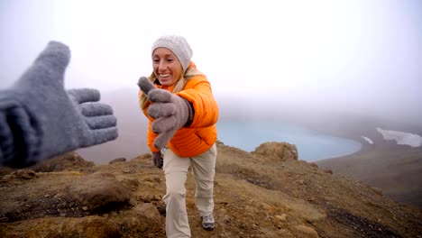 Young-woman-hiking,-pulls-out-hand-to-reach-the-one-of-teammate.-A-helping-hand-to-reach-the-mountain-top.-Hiker-assists-teammate-to-reach-mountain-top-above-volcanic-crater-lake-in-Iceland