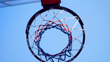 Basketball-bumping-into-hoop-and-passing-through-ring,-outdoor-gym-with-blue-sky-above