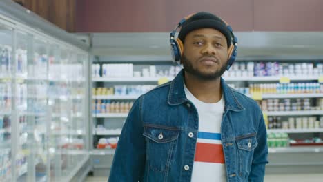 At-the-Supermarket:-Stylish-African-American-Guy-with-Headphones-Walks-Through-Frozen-Goods-Section-of-the-Store.-Following-Back-View-Shot.-Slow-Motion.