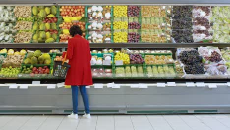 En-el-supermercado:-mujer-elige-producen-de-frutas-orgánicas-en-fresco-de-la-sección-de-la-tienda.-Ella-recoge-melón-y-pone-les-en-su-cesta-de-la-compra.-Vista-trasera-del-tiro.