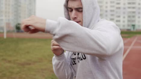 Man-in-hoodie-boxing-with-invisible-opponent-at-stadium.-Young-man-training