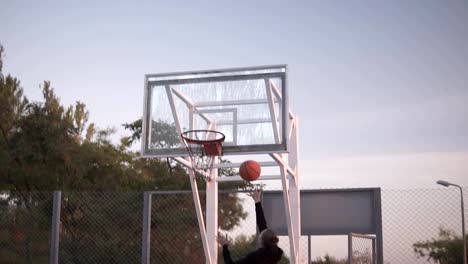 Backside-footage-of-a-young-girl-basketball-player-training-and-exercising-outdoors-on-the-local-court.-Dribbling-with-the-ball,-bouncing-and-make-a-shot