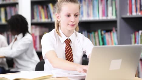 Estudiante-de-secundaria-de-la-mujer-usando-uniforme-trabajando-en-ordenador-portátil-en-la-biblioteca