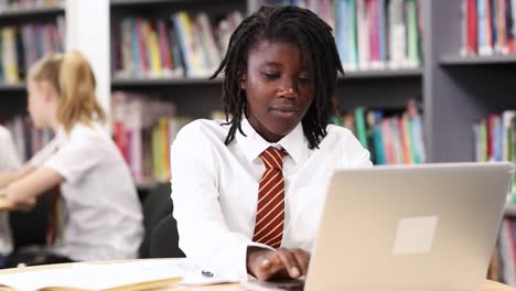 Female-High-School-Student-Wearing-Uniform-Working-At-Laptop-In-Library