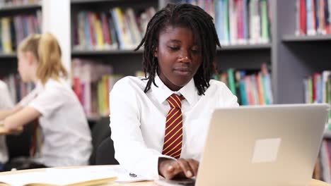 Estudiante-de-secundaria-de-la-mujer-usando-uniforme-trabajando-en-ordenador-portátil-en-la-biblioteca