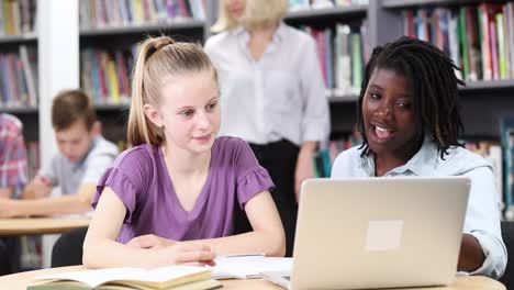 Lehrer-helfen-zwei-weibliche-Schülerinnen-und-Schüler-arbeiten-am-Laptop-In-der-Bibliothek